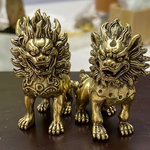May include: Two brass lion statues with detailed manes and fierce expressions. The statues are in a standing position, with intricate detailing on their bodies and paws. The overall design suggests a cultural or decorative theme.
