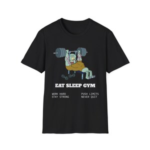 Puede incluir: Camiseta negra con un personaje de dibujos animados levantando pesas, con el texto "EAT SLEEP GYM". El texto adicional incluye "WORK HARD, STAY STRONG" y "PUSH LIMITS, NEVER QUIT". El diseño es en tonos verdes, beige y grises.