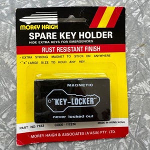 May include: A spare key holder by Morey Haigh, with a rust-resistant finish. The black magnetic key holder is labeled "KEY-LOCKER" and is designed to hide extra keys for emergencies. The packaging is black, red, and yellow.