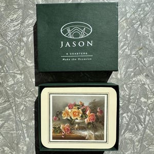 May include: A set of six coasters in a dark green box. The coasters feature a floral still life with pink and yellow roses. The box is labeled "JASON" and includes the text "6 COASTERS" and "Make the Occasion."