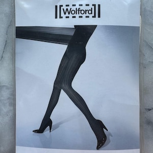 Op de afbeelding: Een verpakking zwarte Wolford Yale panty's. De panty's zijn geribbeld en worden getoond op een model dat zwarte hoge hakken draagt. De verpakking is wit met het Wolford-logo en de woorden "YALE TIGHTS". De verpakking is gemarkeerd met "LARGE".