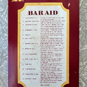 May include: A vintage "Deluxe Bar Set" card featuring cocktail recipes such as Alexander No. 1 and Gin Fizz. The card has a red and gold design, with the words "BAR AID" in large letters. Made in Japan.