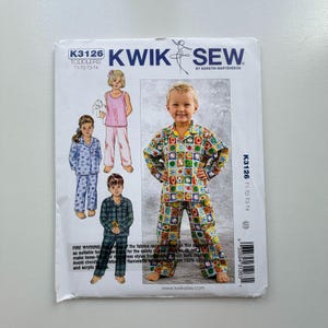 May include: Kwik Sew toddler's pajama pattern. The pattern features illustrations of children wearing different pajama sets. The cover shows a child in a colorful soccer ball print pajama set. The pattern includes sizes 11-12-13-14.