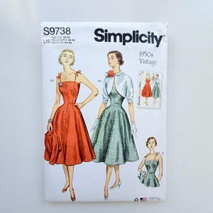 Op de afbeelding: Een Simplicity S9738 naaipatroon-envelop voor jurken in 1950s vintage stijl. De witte papieren hoes bevat illustraties van twee jurken: een effen oranje jurk met dunne bandjes en een groen-witte gingham geruite jurk met een wit bolerojasje.