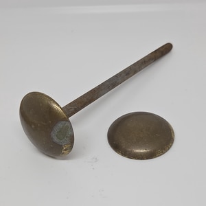 May include: Two brass-toned upholstery nails with rounded, domed heads. One nail features a long, straight, weathered metal shaft attached to the head, while the other is a separate, detached domed cap with a tarnished, aged metallic finish.