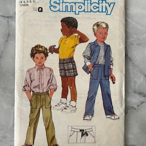 Puede incluir: Sobre de patrón Simplicity vintage, talla N para Niños. La portada presenta ilustraciones de diseños de ropa infantil, incluyendo una camisa con cuello, pantalones cortos y pantalones. El logotipo de Simplicity es azul, con el número de patrón 6719.