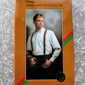 Puede incluir: Caja marrón con foto de una persona con tirantes. La caja tiene un patrón de diamantes y el texto "25mm Adult multi fit size for UK". Los tirantes son marrones con un diseño estampado.