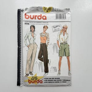 Peut inclure: Une pochette de patron de couture Burda, numéro 3098, illustrant trois styles de pantalons : un pantalon beige, un pantalon cargo marron foncé et un bermuda vert olive. L'enveloppe en papier blanc comporte du texte et un code-barres.