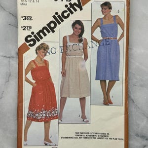 May include: A vintage Simplicity sewing pattern envelope showing three dress designs. The envelope features the text "Simplicity" and "Overnight Success". The dresses are in red, beige, and blue, with floral and solid patterns.