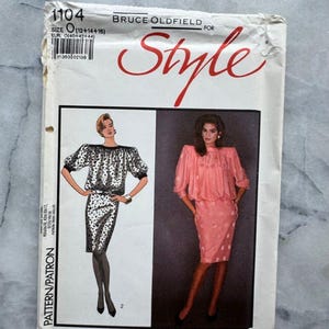 May include: A vintage dressmaking pattern, featuring illustrations of two dress designs. The pattern is labelled "1104" and includes the text "BRUCE OLDFIELD FOR Style". The pattern is printed on white paper with a marble background.