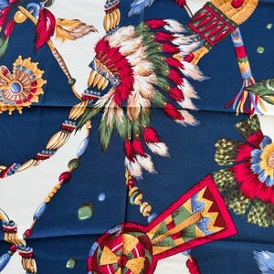 Könnte beinhalten: Ein quadratisches Tuch mit einem von amerikanischen Ureinwohnern inspirierten Design. Das Tuch hat einen marineblauen Hintergrund mit weißen Abschnitten. Das Design umfasst bunte Federn, Perlen und geometrische Formen in Rot, Gelb und Grün.