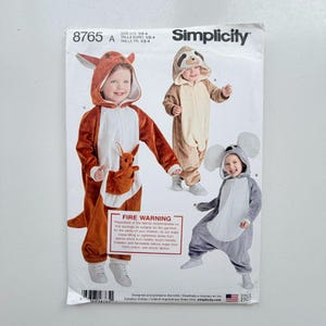 May include: A Simplicity 8765 sewing pattern envelope for children's animal costumes in sizes 1/2-4. The cover features illustrations of three hooded jumpsuits: a brown kangaroo with a joey in a pouch, a tan sloth, and a grey koala with large ears.