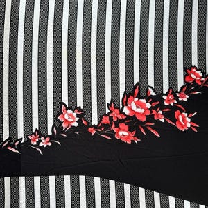 May include: A fabric featuring a pattern of vertical black and white stripes alternating with dotted stripes. A large, solid black section cuts across the fabric diagonally, decorated with a vibrant floral print of red and white flowers and leaves.