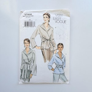 May include: A Very Easy Vogue sewing pattern envelope V7998 featuring illustrations of three variations of a wrap-style top with long sleeves, a wide collar, and a tie-waist detail. The white paper envelope includes a barcode and size label.
