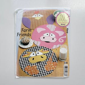 May include: A sewing pattern envelope titled Farm Friends by Ellie Mae Designs K217. The cover features three circular fabric projects: a plaid chicken, a pink pig, and a black and white houndstooth cow with orange floral patches.