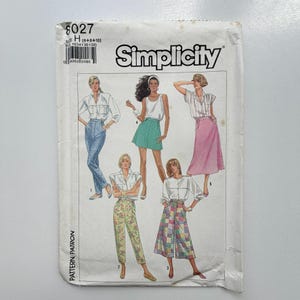 Può includere: Cartamodello Simplicity 8027, taglia H (6+8+10), con illustrazioni di cinque diversi outfit tra cui camicette, pantaloni, una gonna e culotte. La busta di carta bianca mostra varie combinazioni di abbigliamento con motivi floreali, a pois e patchwork.