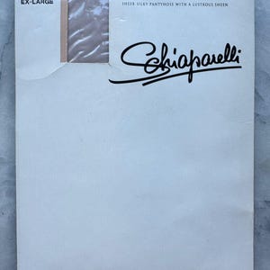 May include: A package of Schiaparelli cashmere pantyhose in an off-white box. The text on the box reads "RAVISANT PANTYHOSE SHEER SILKY PANTYHOSE WITH A LUSTROUS SHEEN" and "CASHMERE EX-LARGE". The pantyhose are visible through a clear window.