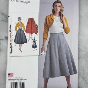 Könnte beinhalten: Simplicity Vintage-Schnittmuster der 1950er Jahre, Größe 42-50. Das Schnittmuster zeigt eine Frau in einem grauen Rock und einer gelben Bolerojacke. Das Muster enthält Illustrationen des Outfits und das Simplicity-Logo.