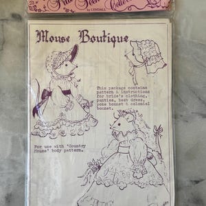 May include: A package from "The Frill Seekers Collection" with illustrations for a "Mouse Boutique." It contains patterns and instructions for bride's clothing, panties, a best dress, a poke bonnet, and a colonial bonnet.