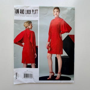 Könnte beinhalten: Ein Vintage-Schnittmuster von Tom und Linda Platt für Vogue Patterns. Das Muster zeigt ein rotes Kleid mit hohem Ausschnitt und langen Ärmeln. Die Musternummer ist V1565, und die Größen sind 6-8-10-12-14.
