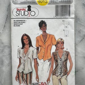 Könnte beinhalten: Ein Burda Studio Schnittmusterpaket mit Illustrationen von Blusen und Westen. Das Paket trägt die Nummer 4013 und den Text "BLUSENWESTE/GILET-BLOUSE/WAISTCOAT/BLOUSE". Die Illustrationen zeigen Frauen in verschiedenen Oberteilen.