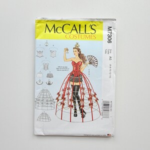 Op de afbeelding: McCall's Costumes naaipatroon M7306, maat A5 (6-8-10-12-14). De envelop bevat een illustratie van een persoon in een rood korset, een zwarte rok en een rood kooimodel crinoline rokframe versierd met kleine strikjes, die een waaier vasthoudt.