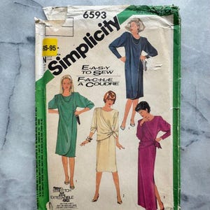 May include: A vintage Simplicity sewing pattern envelope, showing illustrations of four dress designs. The envelope is green and white, with the Simplicity logo and the text "E-A-S-Y TO SEW". The pattern number is 6593.