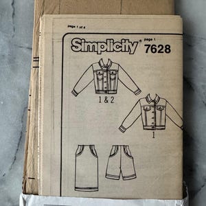 May include: A vintage Simplicity sewing pattern, model 7628, featuring illustrations of a jacket, skirt, and shorts. The pattern is printed on tan paper and includes size charts and instructions. The cover displays the Simplicity logo.