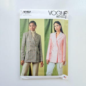 May include: Vogue Patterns V1927 sewing pattern envelope featuring two double-breasted blazer designs. One blazer is a brown and black plaid print, and the other is a solid light pink. Both jackets feature notched lapels, flap pockets, and buttons.
