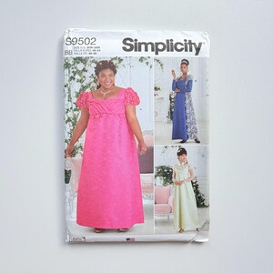 May include: A Simplicity S9502 sewing pattern envelope for sizes 20W-28W. The front displays three variations of a floor-length dress with short puffed sleeves and a square neckline, shown in bright pink, blue with white lace, and cream fabric.