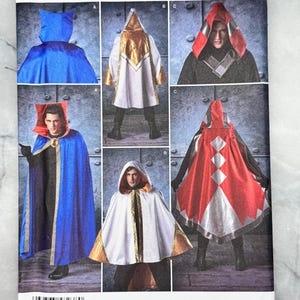 May include: Simplicity sewing pattern 8238 showing costume capes with hoods. The pattern includes designs in blue, white, gold, and red. The package has the text "U.S. ONE SIZE" and "Simplicity".