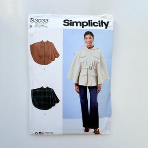 May include: Simplicity sewing pattern S3033 for a hooded cape with a belted waist and four front pockets. The pattern envelope displays three variations: a solid brown cape, a dark green plaid cape, and a cream-colored cape worn with jeans.