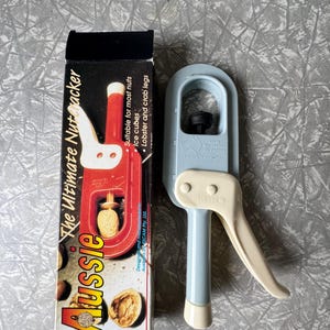 Può includere: Uno schiaccianoci Aussie con un design rosso e bianco, e uno schiaccianoci azzurro con un manico color crema. La scatola recita "The Ultimate Nutcracker" e "Adatto alla maggior parte delle noci, cubetti di ghiaccio, aragosta e zampe di granchio."