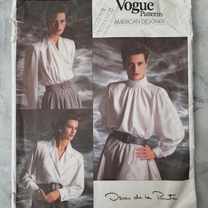 May include: A vintage Vogue Patterns sewing pattern by Oscar de la Renta. The pattern cover shows a woman in a white blouse and grey skirt. The text on the cover reads "Vogue Patterns AMERICAN DESIGNER" and "Oscar de la Renta".