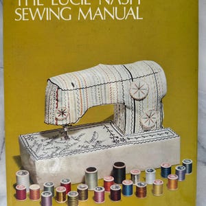 Puede incluir: Un manual de costura vintage titulado "The Lucie Nash Sewing Manual" con una ilustración estilizada de una máquina de coser. La imagen presenta un fondo amarillo, una máquina de coser blanca con costuras coloridas y carretes de hilo.