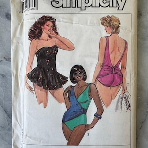 Könnte beinhalten: Ein Vintage-Simplicity-Schnittmusterpaket mit Illustrationen von drei Badeanzügen. Das Paket ist weiß mit dem Simplicity-Logo und dem BBW-Logo. Die Badeanzüge sind in Schwarz, Rosa und Türkis gehalten.