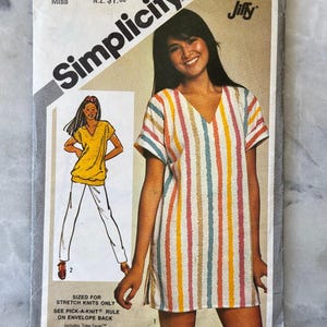 May include: A vintage Simplicity sewing pattern, size small 10-12 Miss. The pattern shows a woman in a striped V-neck dress. There is also a drawing of a yellow top and white trousers. The pattern includes the text "Simplicity" and "Jiffy".