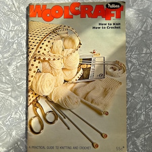 May include: A vintage "Woolcraft" magazine with orange and white text, detailing knitting and crochet techniques. The image shows yarn, knitting needles, scissors, and a measuring tape, indicating a crafting theme.