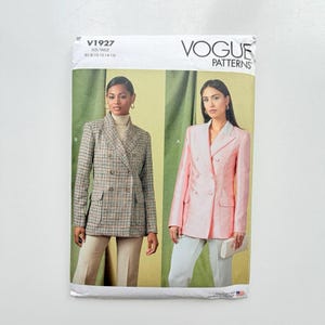 Op de afbeelding: Vogue Patterns V1927 naaipatroon-envelop met twee dubbelrijige blazerontwerpen. De ene blazer heeft een bruin en zwart ruitpatroon en de andere is effen lichtroze. Beide jasjes zijn voorzien van reverskragen en klepzakken.