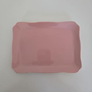 Puede incluir: Una bandeja rectangular con un acabado liso y sólido en color rosa empolvado. La bandeja presenta un diseño de borde curvo ligeramente elevado que crea un contorno suave y ondulado alrededor de la superficie central plana y sencilla.