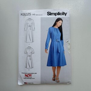 May include: Simplicity sewing pattern K9225 for a dress with a belt. The pattern includes illustrations of the dress design and a photo of a woman wearing the dress. The pattern is size U.S. 6-14.