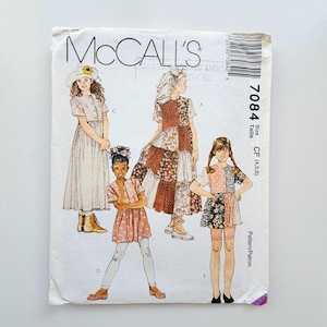 Könnte beinhalten: Ein McCall's 7084 Schnittmusterumschlag mit Illustrationen von vier verschiedenen Kleiderstilen, die mit A, B, C und D gekennzeichnet sind. Der weiße Papierumschlag zeigt den Markennamen, die Nummer 7084, Größe CF (4,5,6) und einen Strichcode.