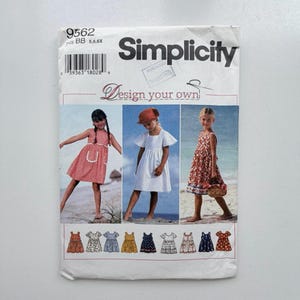 Op de afbeelding: Een Simplicity naaipatroon-envelop, nummer 9562, voor kinderjurken in de maten BB 5, 6, 6X. De omslag toont drie foto's van kinderen in verschillende jurkstijlen, samen met illustraties van negen variaties aan de onderkant van de verpakking.