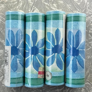May include: Four rolls of wallpaper with a blue floral design. The wallpaper features large blue flowers on a light blue background with a green and blue plaid border. The rolls are cylindrical and stacked together.