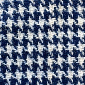 Puede incluir: Primer plano de una tela tejida con un patrón de pata de gallo clásico. La tela presenta un diseño repetitivo de formas blancas y azul marino, creando una apariencia texturizada. El patrón está tejido apretado, lo que sugiere un material duradero.