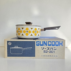 May include: A white saucepan with a repeating yellow and black starburst pattern, a brown lid knob, and a silver handle. It sits on a blue and white cardboard box labelled SUNCOOK, S2-201, and Japanese text. The box features a line drawing of the pan.