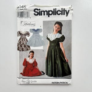 Könnte beinhalten: Ein Simplicity Schnittmusterumschlag 5145, Größe AA (7-10), mit Abbildungen und Fotos von Kleidern mit Puffärmeln und großen Kragen. Die Packung zeigt drei Kleiddesigns in floralem, gestreiftem und einfarbig dunkelgrünem Stoff.