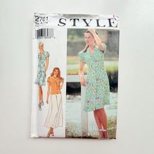 May include: A Style brand sewing pattern envelope, number 2701, featuring illustrations of a floral print dress and a separate top and skirt combination. The packaging displays the text STYLE, the pattern number 2701, and a barcode.