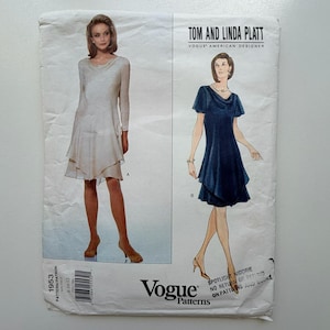 Peut inclure: Un patron de couture vintage Vogue Patterns avec des illustrations de deux modèles de robes. Une robe est blanche, l'autre bleu marine. Le patron est de Tom et Linda Platt, designers américains. Le logo Vogue est visible.