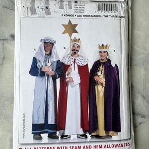 Op de afbeelding: Een naaipatroonpakket met illustraties van drie koninklijke kostuums. Het pakket bevat de tekst "3 Könige - Les Trois Mages - The Three Magi" en het nummer "2438". De kostuums omvatten gewaden, capes en kronen.